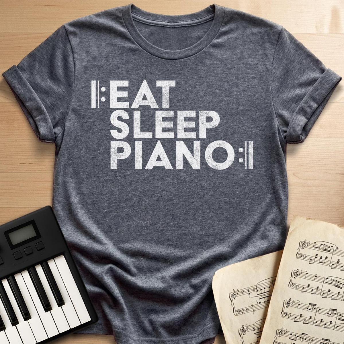 Dark Heather tee with bold “Eat Sleep Piano” text framed by repeat-sign bars, a fun gift for pianists