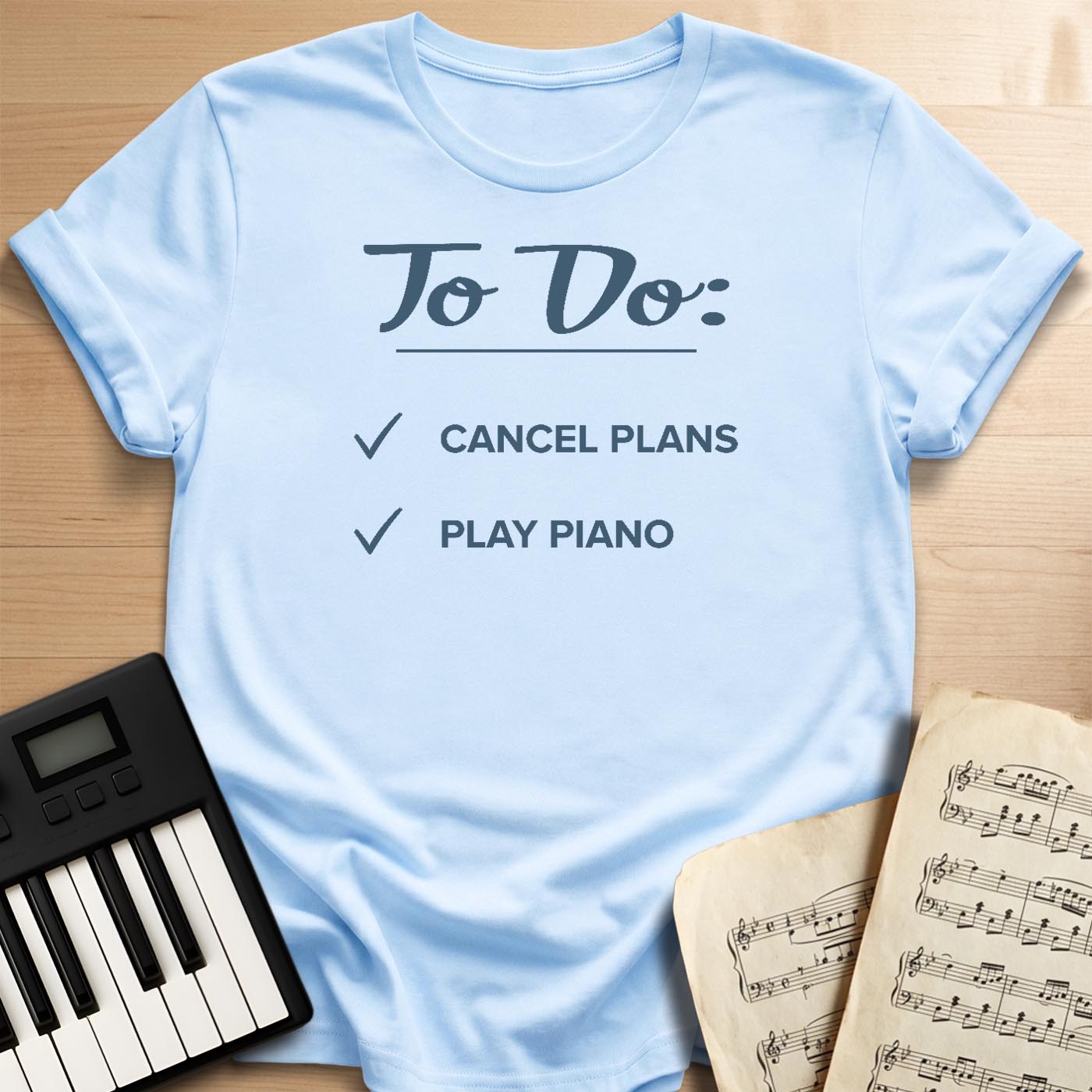 Light blue To Do Cancel Plans Play Piano t-shirt, flat lay with piano keyboard and sheet music